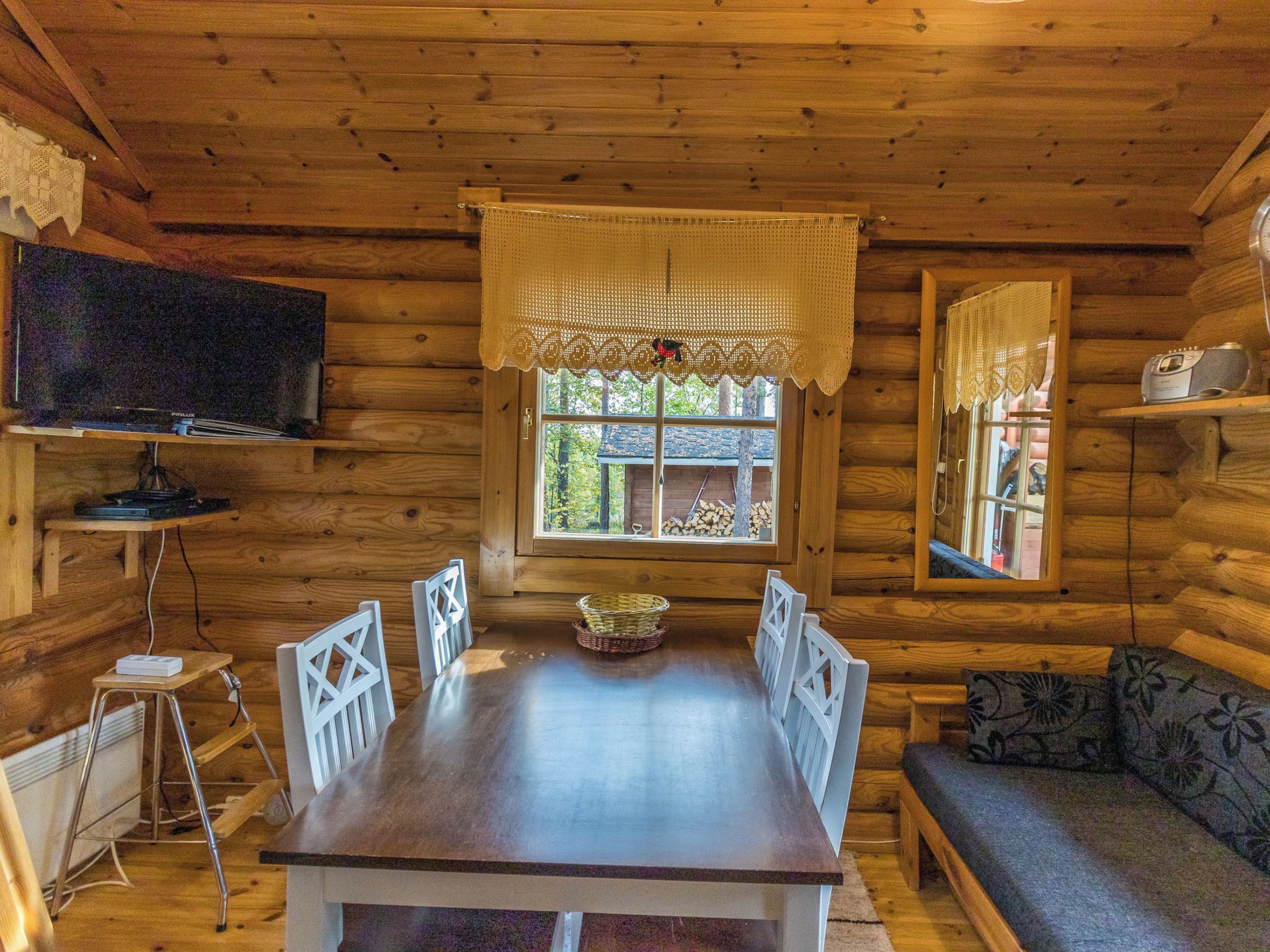 L’intérieur d’une cabane en rondins, avec une table à manger, des chaises, un téléviseur et une fenêtre avec des rideaux.