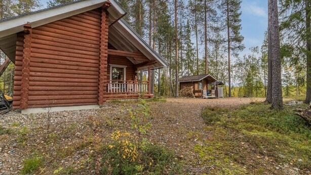 Une cabane en rondins avec un porche et une plus petite cabane située dans une zone boisée.