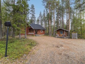 Une cabane avec un porche, une petite cabane séparée et une zone boisée avec un sentier de gravier.