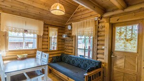 L’intérieur d’un chalet confortable, avec des murs en bois, une table à manger en bois, des chaises, un banc et une grande fenêtre ornée de rideaux en dentelle.