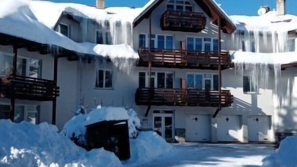 Un immeuble à plusieurs étages, dont le toit et les balcons sont recouverts de neige, et qui est entouré de neige.
