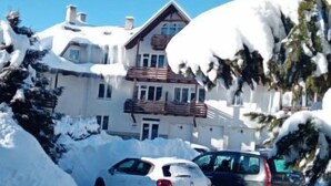 Un bâtiment recouvert de neige, avec une longue allée et des voitures garées.