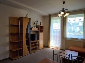 Una habitación con un armario de madera, televisor, mesa de comedor con sillas y ventana con cortinas.
