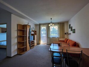 A compact living space with a dining area, a built-in wooden shelving unit, a sofa, and a window with curtains.