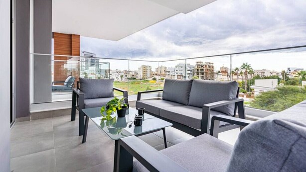 Un balcon moderne avec une table en verre, deux canapés gris et une vue sur le paysage urbain.
