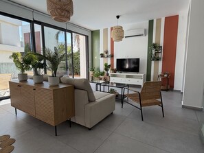 Un salon moderne avec un canapé, un fauteuil et un téléviseur posé sur un meuble blanc.
