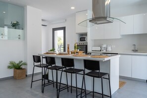 A modern kitchen with white cabinets, a central island with bar stools, a glass backsplash, and a large window.