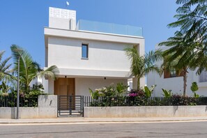 A modern two-story house with a flat roof, a small balcony, and a gated entrance.