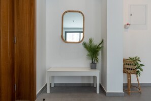 A hallway with a wooden door, a white bench, a mirror, and two wicker chairs with plants.