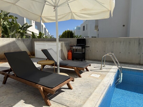 A poolside area with lounge chairs, a barbecue grill, and a gas cylinder.