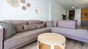 A modern living room with a large L-shaped sofa, a round wooden coffee table, and decorative wall art. - Citrus 3-Bedroom Apartment in Larnaca (Larnaca)