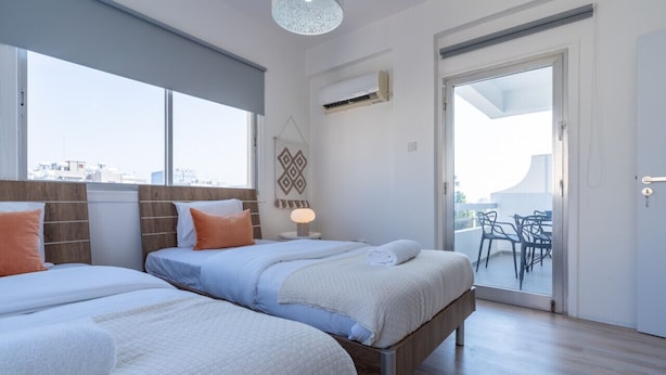 A hotel room with two beds, a balcony with outdoor furniture, and a city view. - Citrus 3-Bedroom Apartment in Larnaca (Larnaca)
