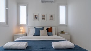 Een keurig opgemaakt slaapkamer met een groot bed, twee nachtkastjes en een wandairconditioner.