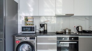 Een kleine keuken met een wasmachine, magnetron, koffiezetapparaat en oven.