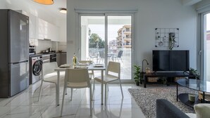 Een modern appartement met een keuken, een eethoek en een woonkamer. Het heeft een groot raam, een flatscreen televisie en een eettafel met stoelen.