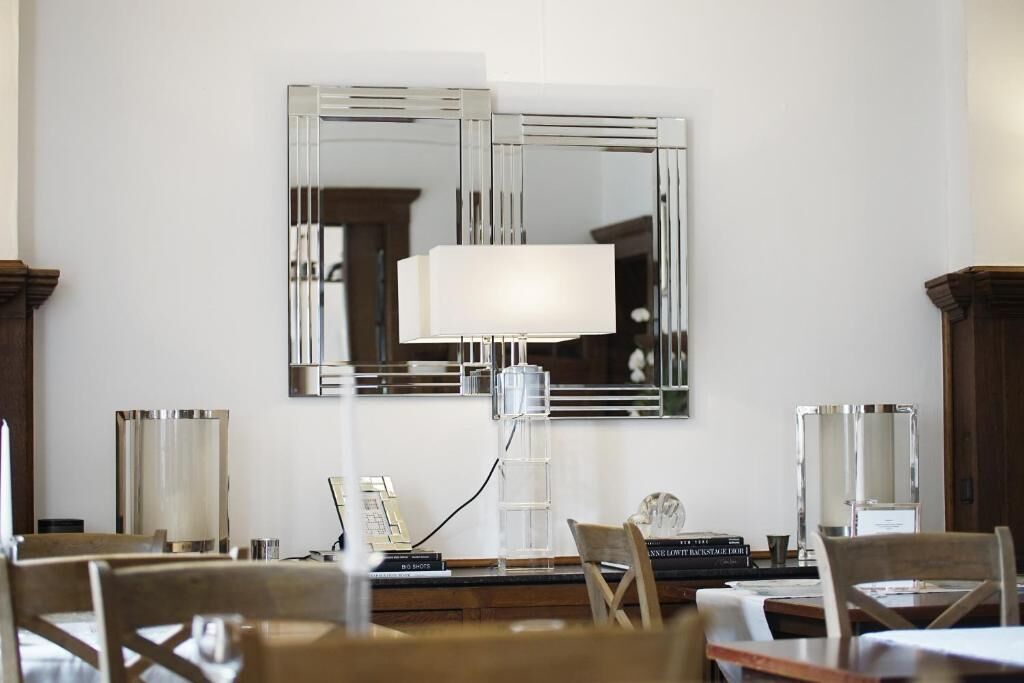 Et spiseområde med et bord dækket til to, en moderne lampe og et stort spejl på væggen.