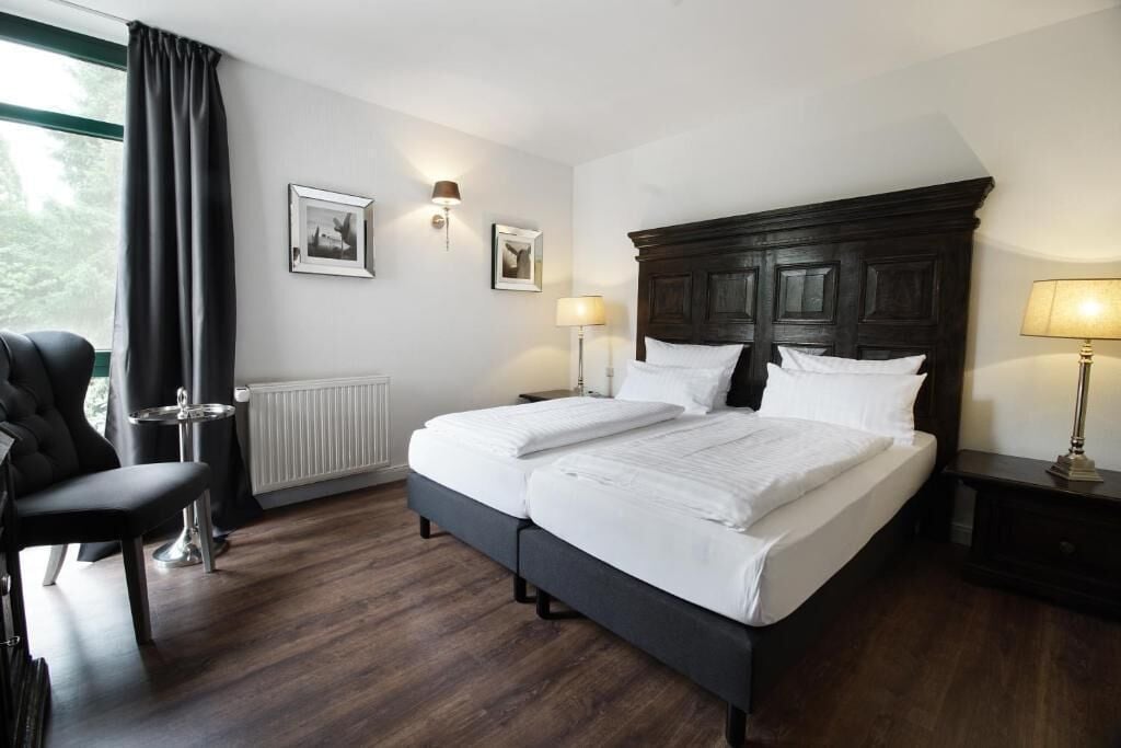 A hotel room with a large bed, a chair, a nightstand, and two wall-mounted lamps.