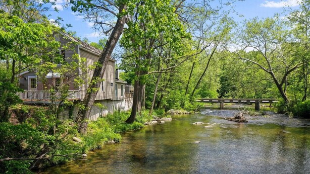 Una casa junto a un arroyo cristalino con un puente de madera.