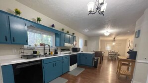 Una cocina con armarios azules, lavavajillas, estufa y comedor con mesa y sillas.