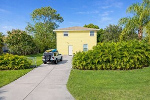 A yellow two-story house with a paved driveway leading to the front door.