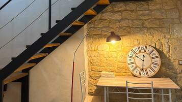 A staircase with a glass railing, a stone wall, a wooden table with chairs, and a wall clock.
