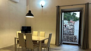 Un comedor con una mesa y sillas, un televisor y vistas a un balcón con edificios.