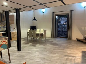 Een modern interieur met een eethoek, een televisie en uitzicht op een stadsgezicht door een deur.