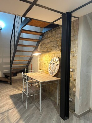 Un cuarto estilo loft con un escritorio de madera, una silla, un reloj, una escalera y una pared de piedra.