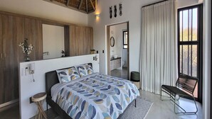 Un dormitorio moderno con una cama grande, cabecera de madera, un espejo, una ventana con cortinas y un banco cerca de la ventana.