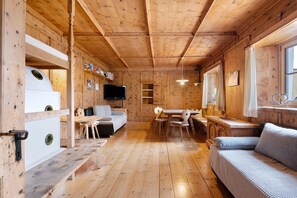 Ein Holzblockbau-Innenraum mit einer Couch, einem Esstisch, Stühlen, einem Fernseher und einem Fenster.