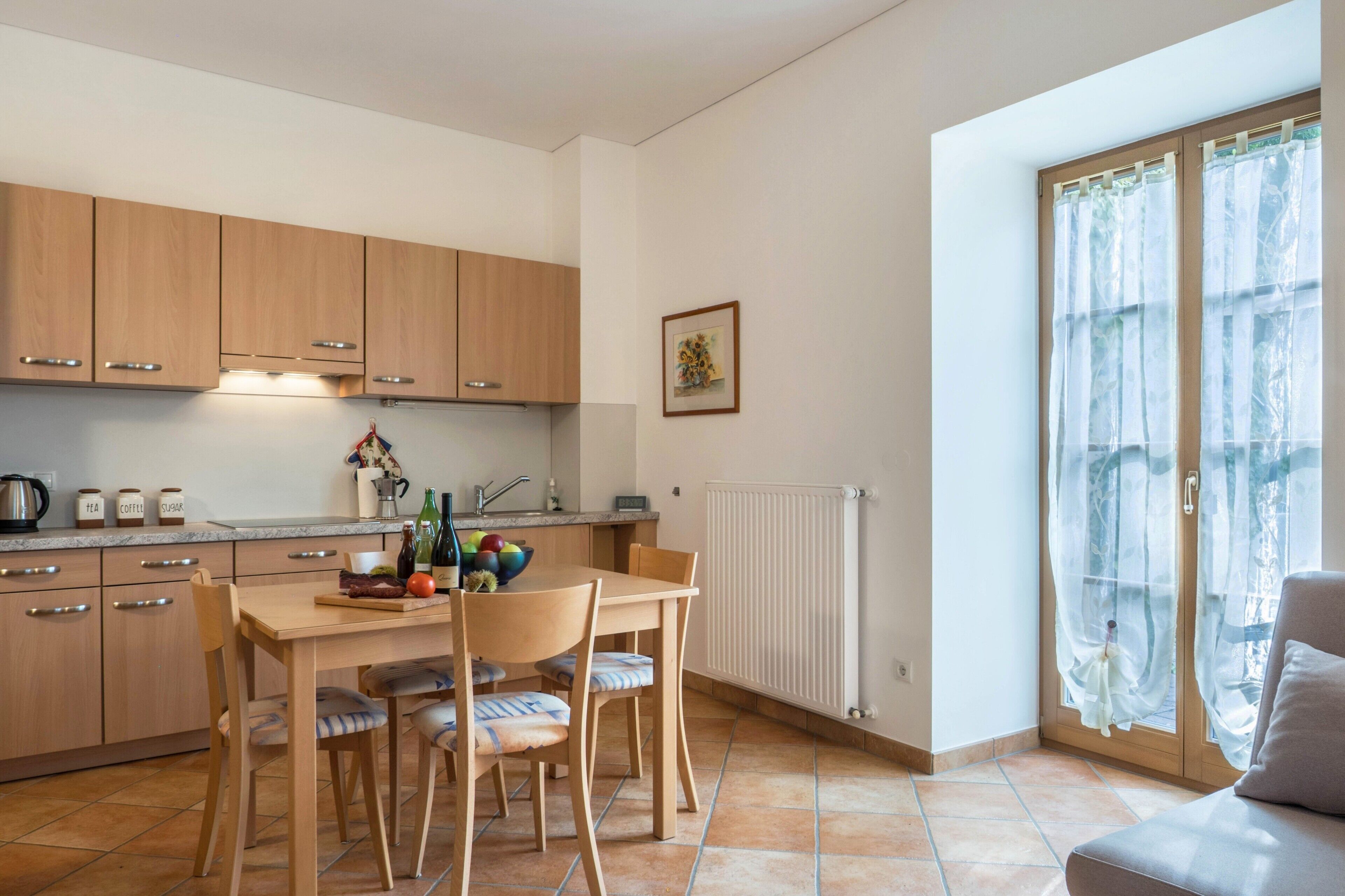 Une cuisine avec des meubles de rangement en bois, une table à manger avec des chaises, un radiateur et une fenêtre avec des rideaux.