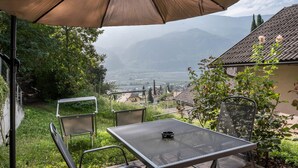 An outdoor patio with a table and chairs, a large umbrella, and a view of distant mountains and a valley. - Apartment 'Linslhof Terlaner' with Mountain View, Private Terrace and Wi-Fi (Terlano)