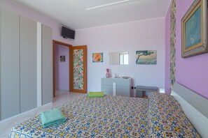 A bedroom with a patterned bedspread, a bedside table with a vase, a mirror, and artwork on the walls.
