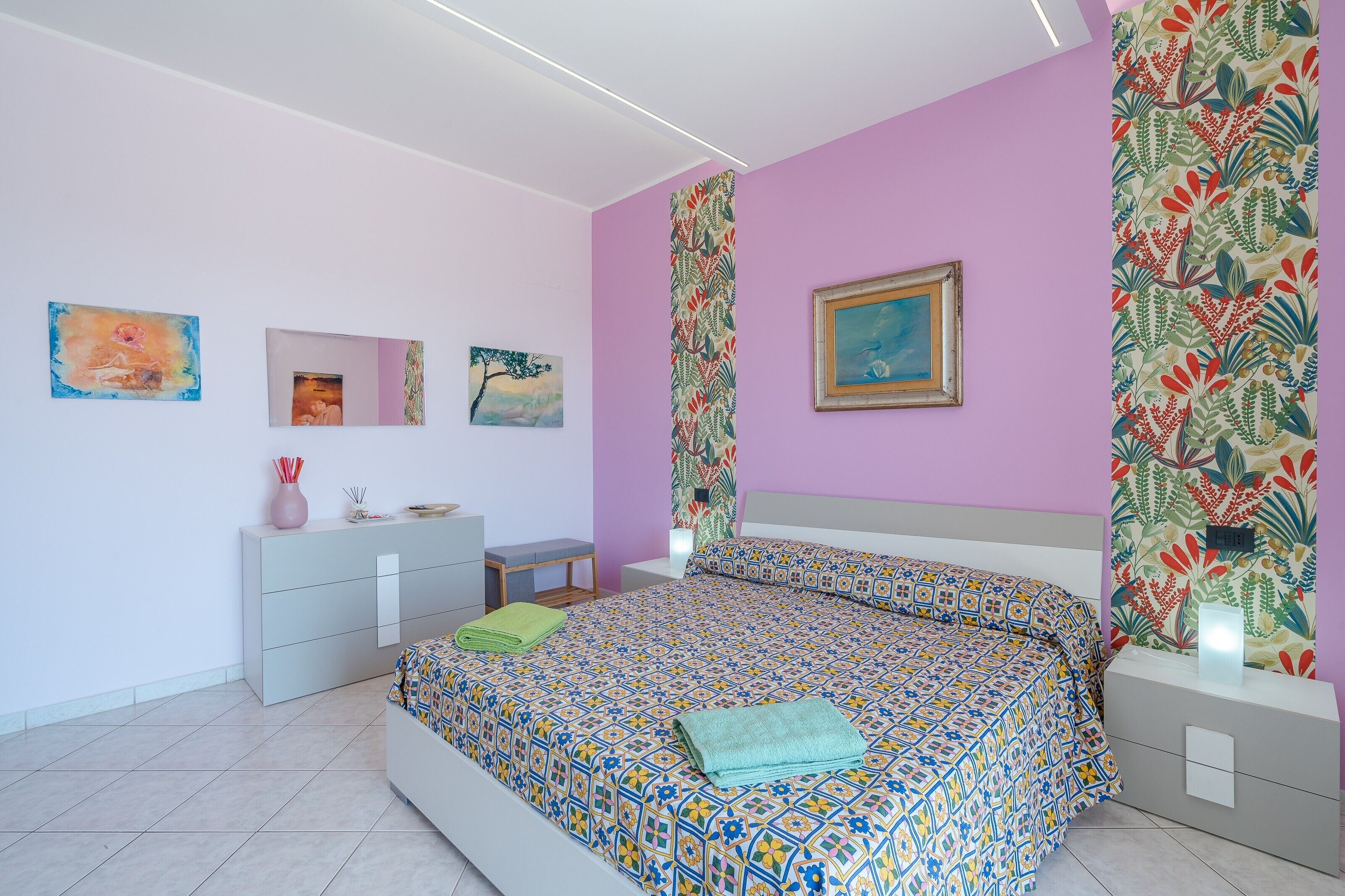A bedroom with a bed, bedside tables, a dresser, and artwork on the walls.