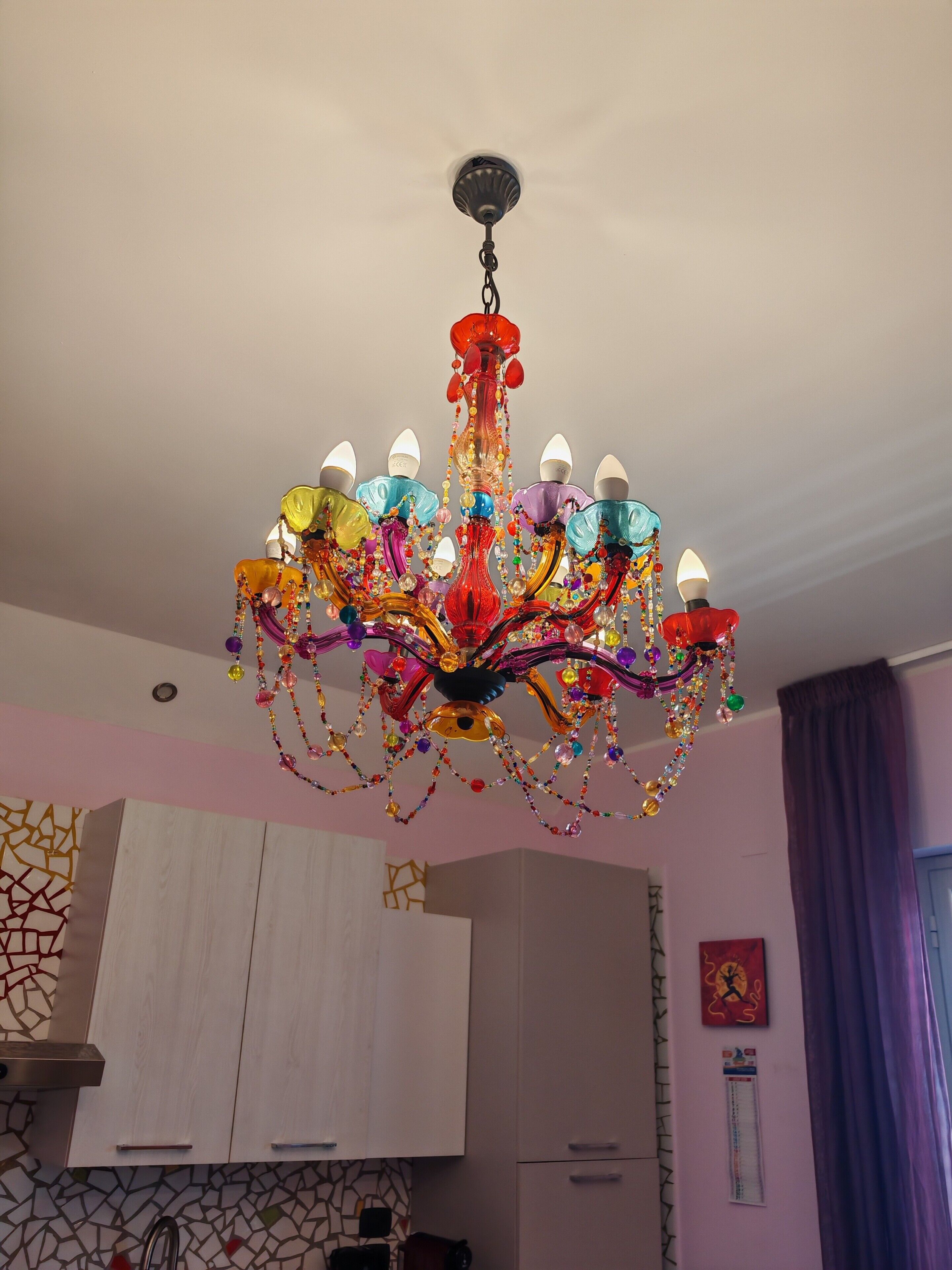 Un lampadari amb diverses llums, armaris blancs i una paret amb dibuixos.
