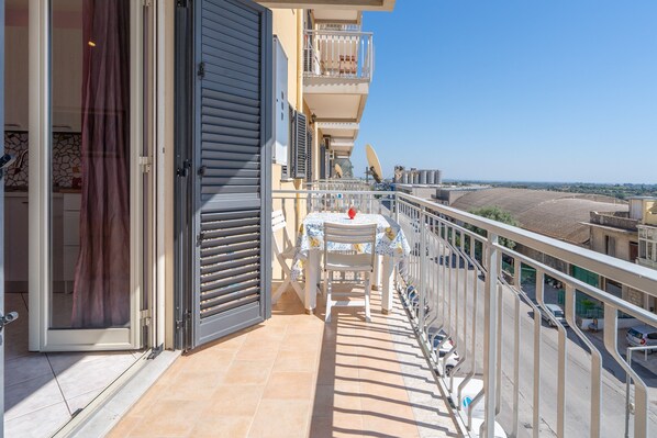 A balcony with a table and chairs, a sliding door, and a view of the street.
