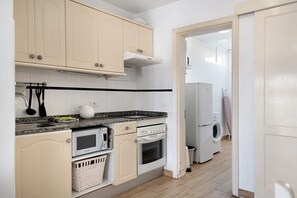 Een keuken met een magnetron, oven en wasmachine, en een deur naar een wasruimte.