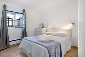 Een slaapkamer met een bed, nachtkastje, raam met gordijnen en een wandlamp.