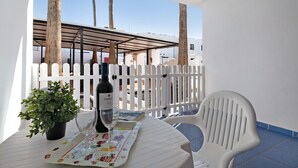Un balcón con una mesa, sillas, una planta en maceta, una botella de vino y una copa.