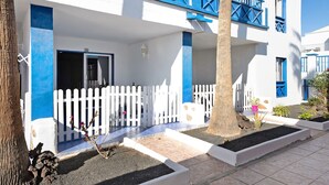 Un edificio blanco con detalles azules, una valla de piquete blanca y una zona de patio con baldosas.