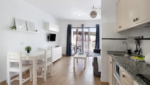 Una cocina moderna con armarios blancos, un comedor con mesa y sillas blancas, y un televisor montado en la pared.
