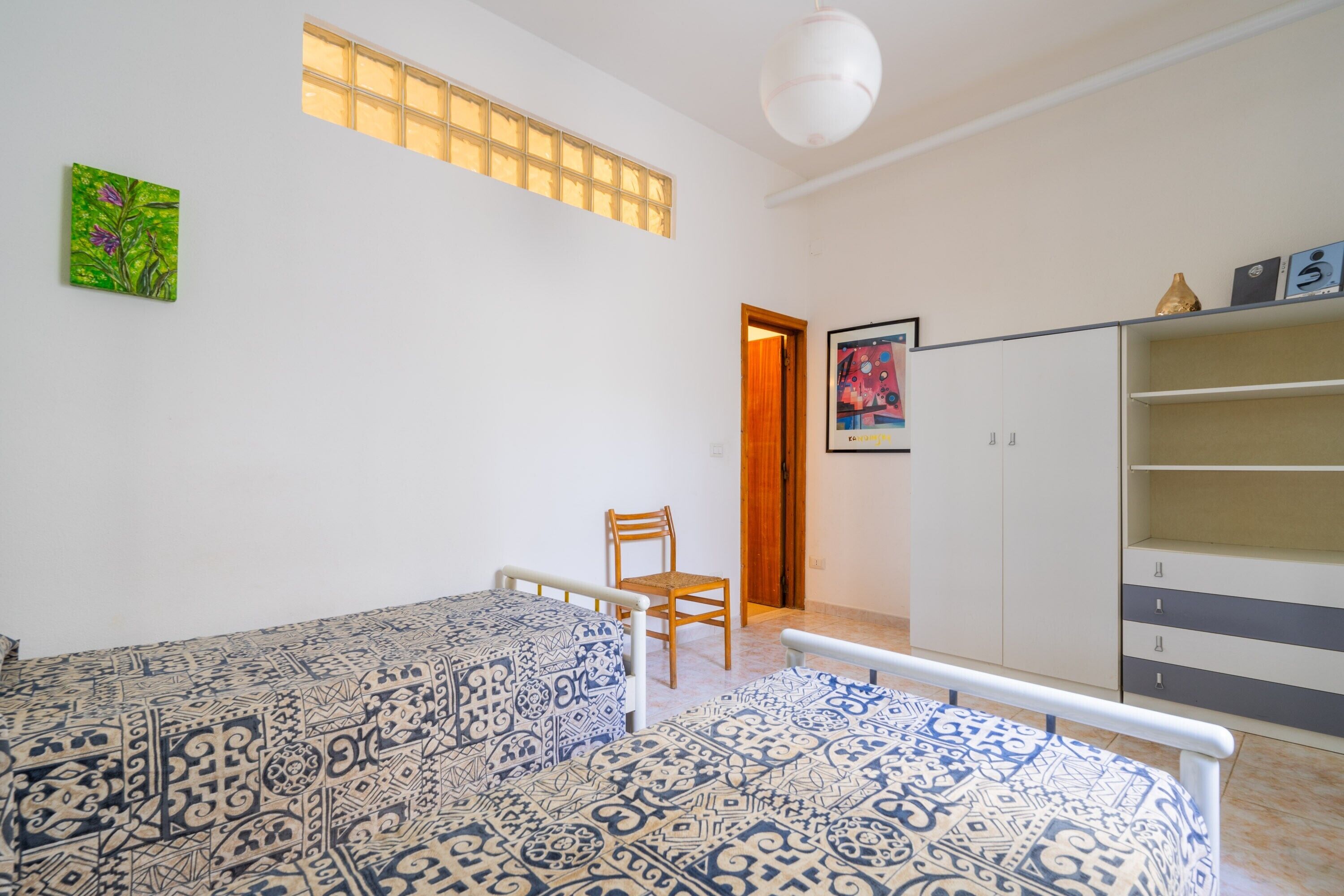 A room with two beds, a chair, a wardrobe, and a window with a view.