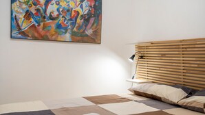 Un dormitorio con cama, cabecera de madera, un cuadro abstracto de colores y una colcha.