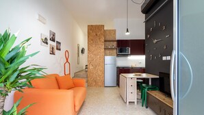Un espacio habitable compacto con kitchenette, un sofá, una mesa de comedor y una silla verde.