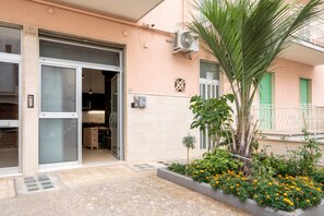 A building with a garage door, a small garden with flowers, and a palm tree.