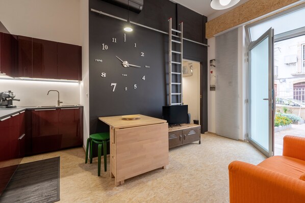 A modern kitchen with a wooden table, a green chair, a TV, and a clock on the wall.