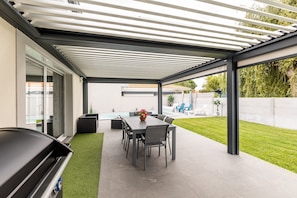 A covered patio with a dining table and chairs, a grill, and a view of a swimming pool and garden. - Villa "Bassin d'Arcachon" with Private Pool, Private Terraces and Wi-Fi (ARES)
