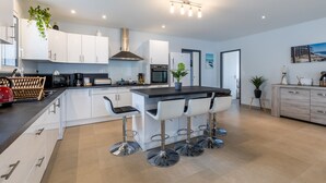 A modern kitchen with white cabinetry, a central island with bar stools, a built-in oven, and a stainless steel range hood. - Villa "Bassin d'Arcachon" with Private Pool, Private Terraces and Wi-Fi (ARES)