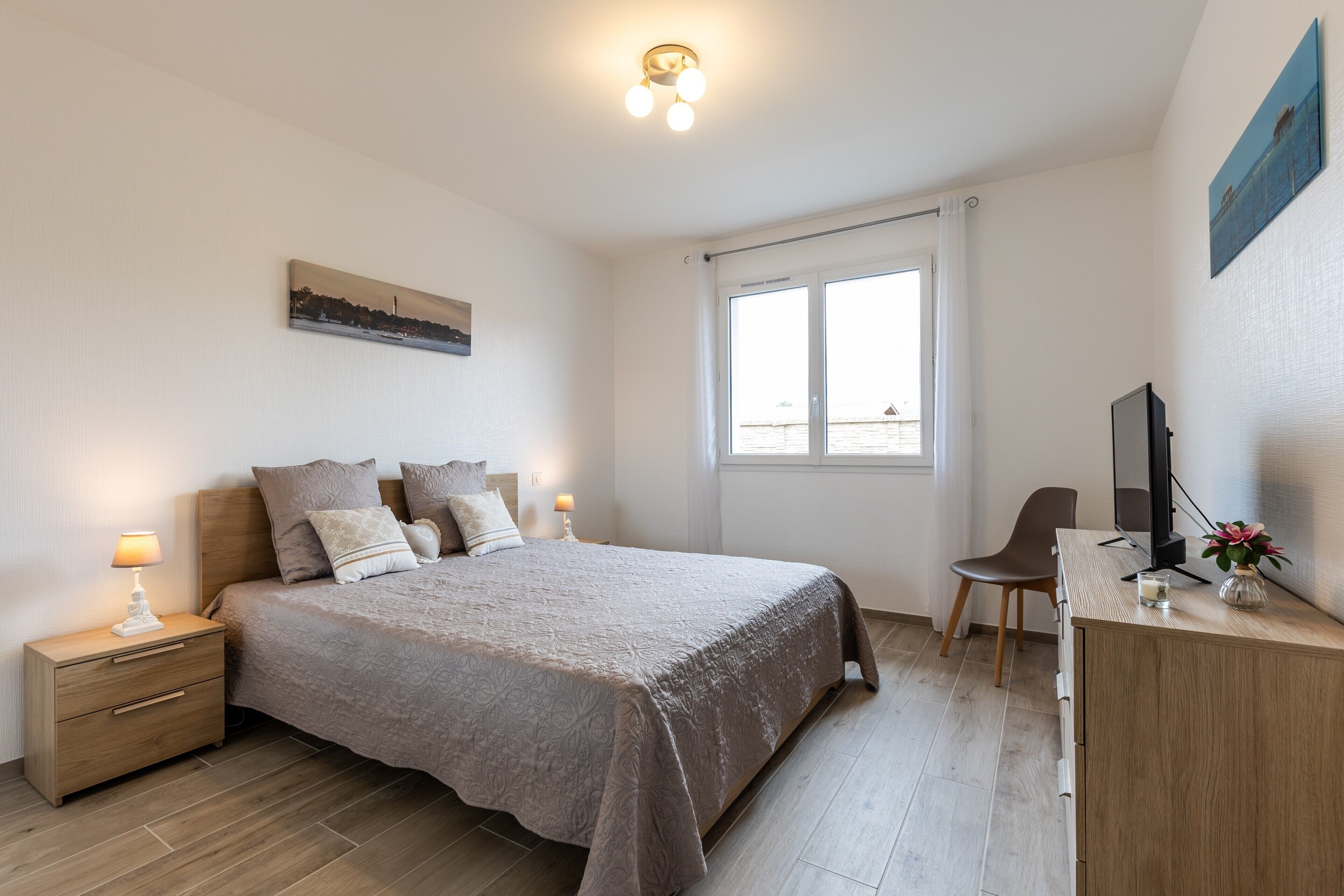 A bedroom with a bed, bedside table, lamp, chair, desk, TV, and a window.