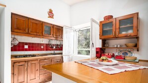 A kitchen with wooden cabinets, a red-tiled backsplash, a large window, and a central island with a placemat. - Holiday Apartment "Casa Su Craminu" with Mountain View, Balcony & Wi-Fi (Dorgali)